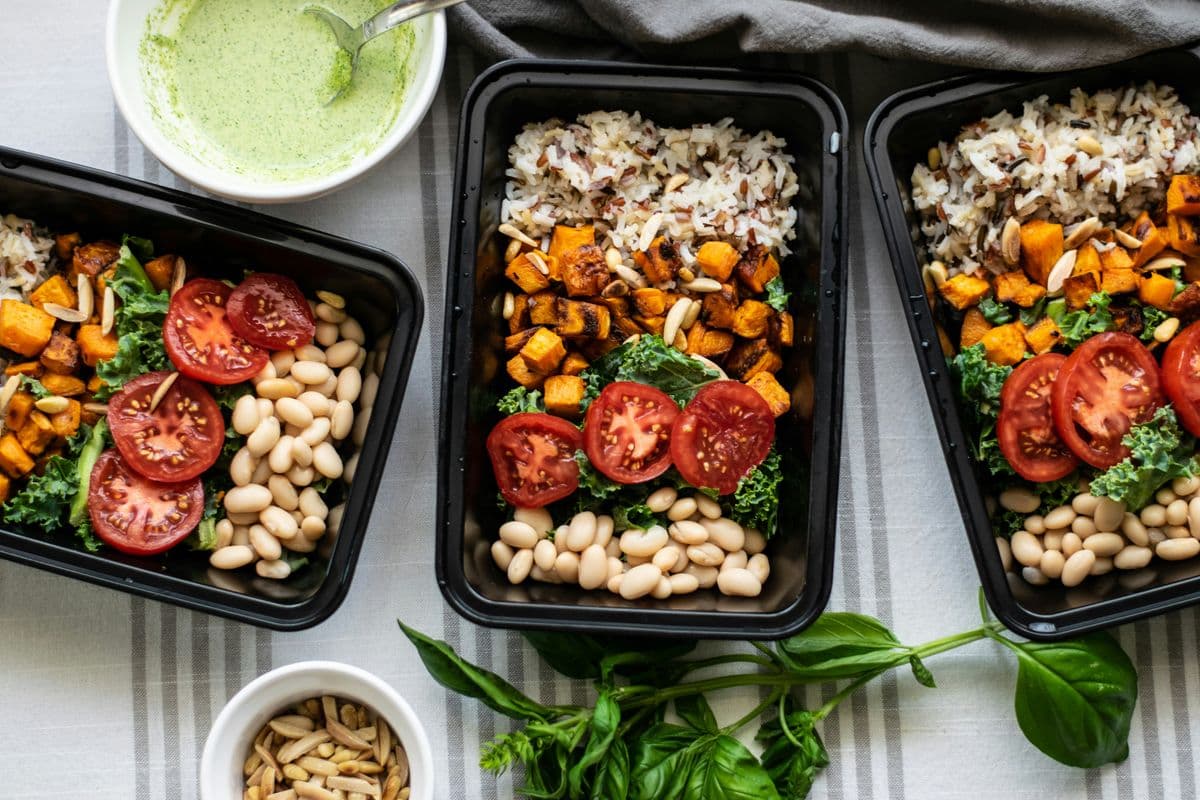 Three portioned meal prep containers with rice, roasted sweet potato, beans, kale and tomatoes for weight loss