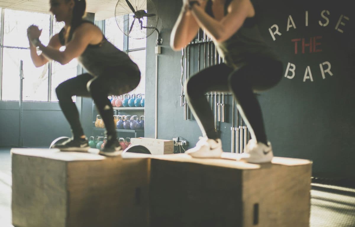 Two people doing box jumps in a CrossFit gym — quick lunchbreak workout