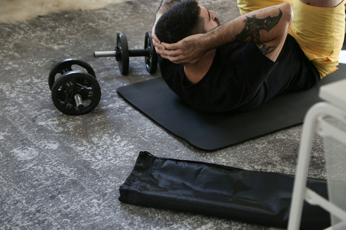 Man doing crunches on a mat with dumbbells nearby during a morning HIIT workout at home