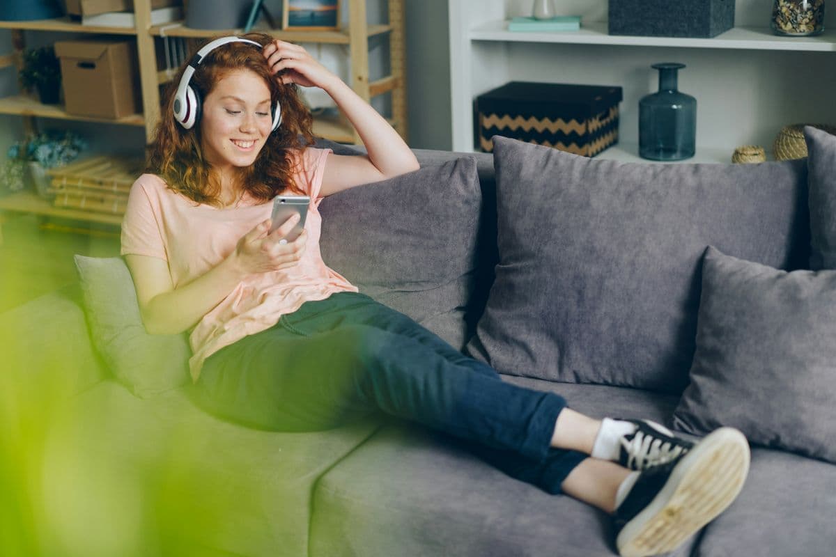 Woman relaxing on the sofa with headphones and phone after work — switching off properly