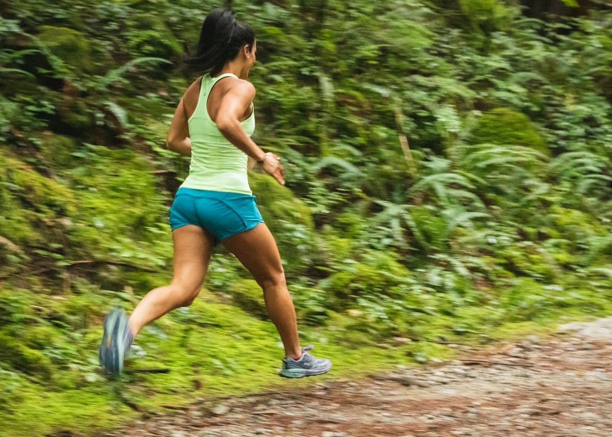 Woman trail running through lush green scenery — physical activity to stop stress eating after work