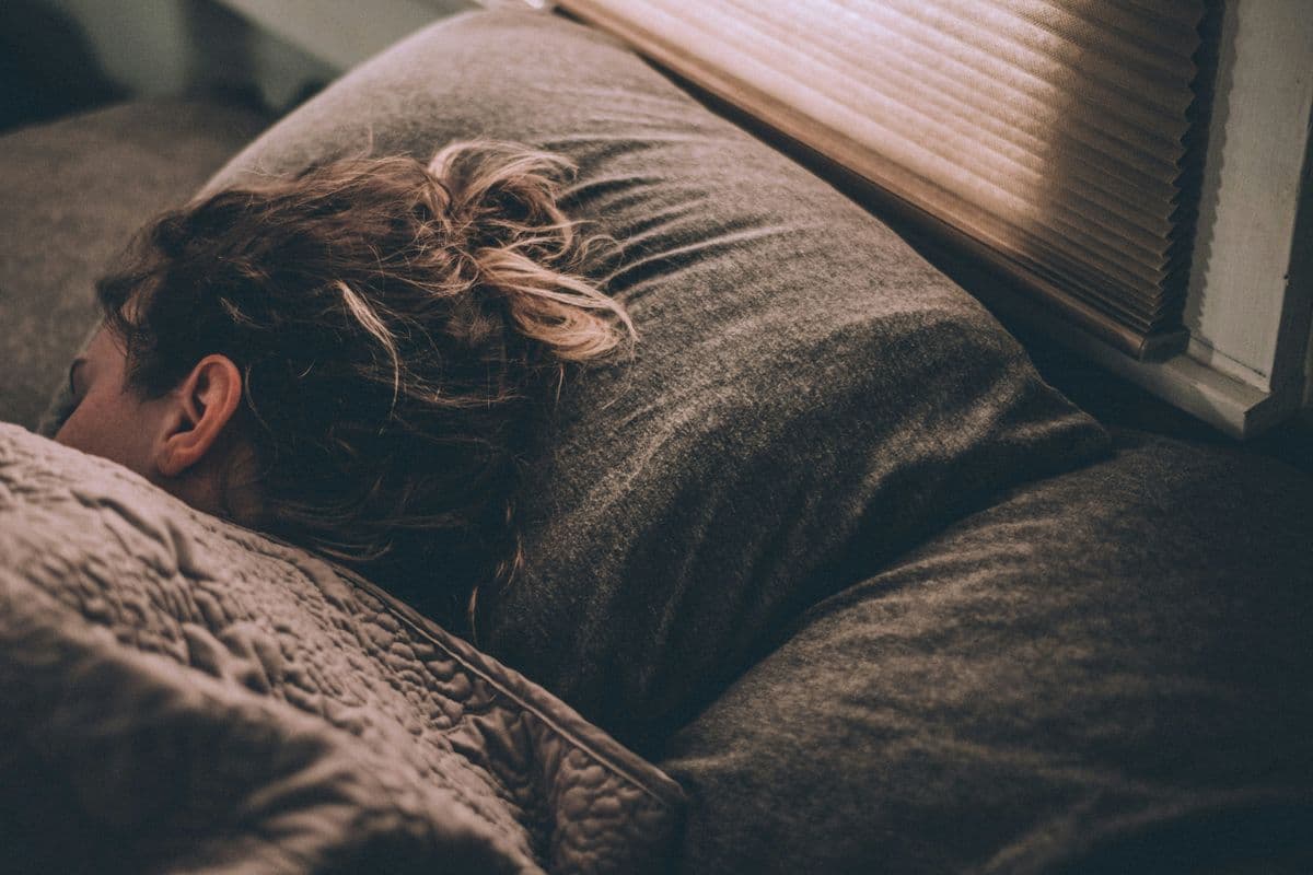 Person sleeping face-down in a pillow after a night shift with daylight filtering through a blind